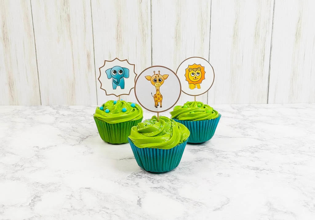 three cupcakes with green frosting and cupcake toppers. Toppers feature a lion, elephant, and giraffe. 