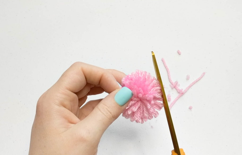 Yarn is being clipped with scissors to even out the pom pom.