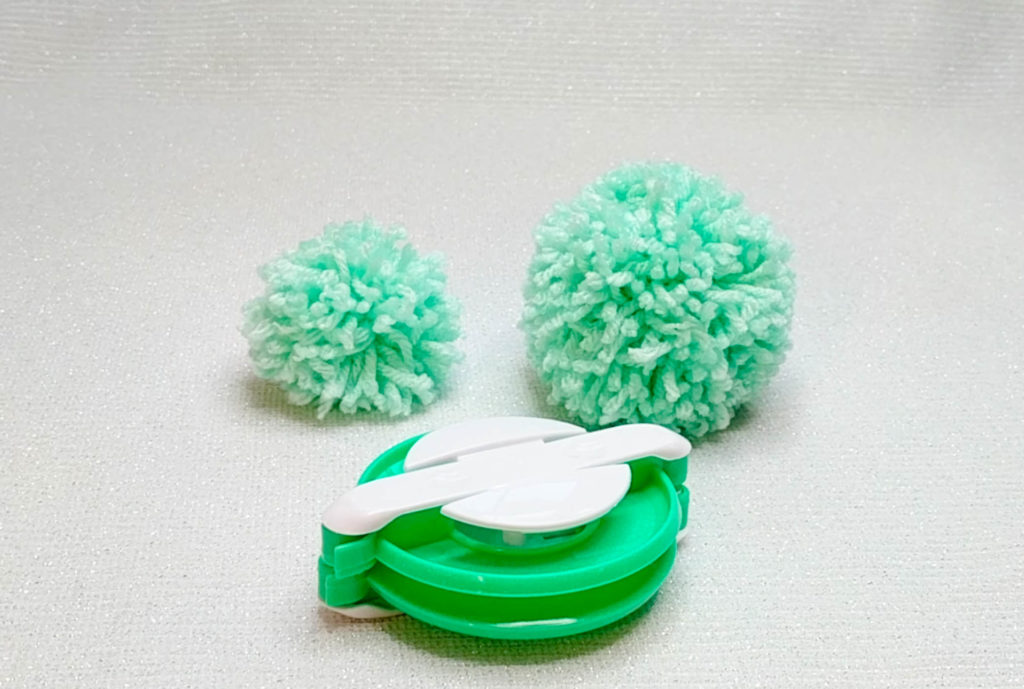 Showing two pom poms of different sizes showcased by the tool that made them