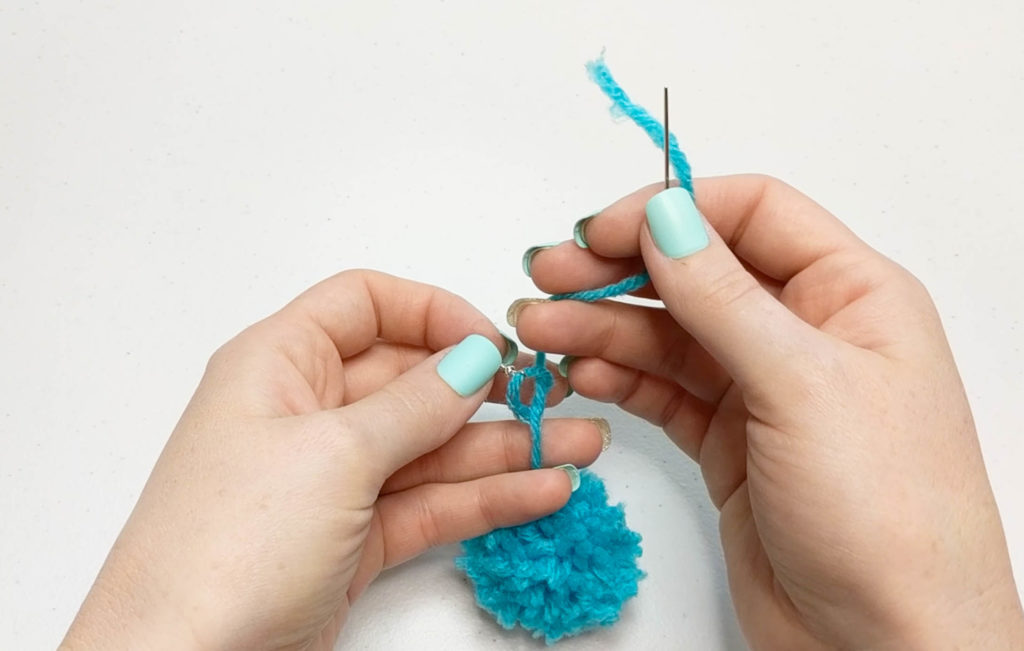 knot being tied on earring hook with the long tail from pom pom.
