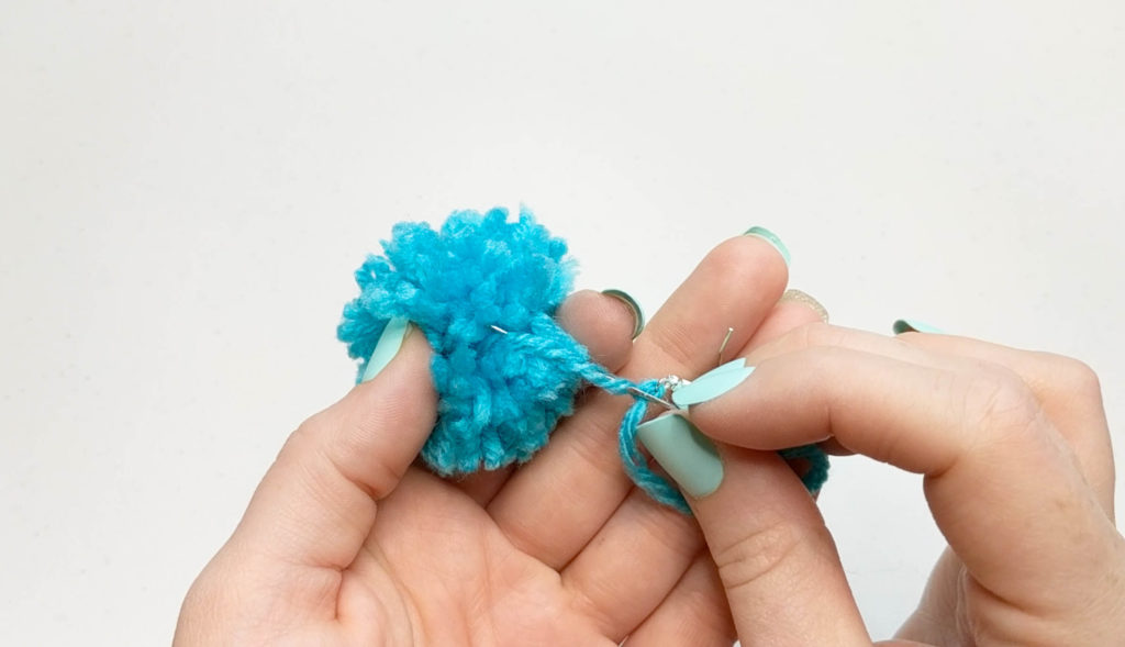 embroidery needle passing back through the string holding the pom pom.