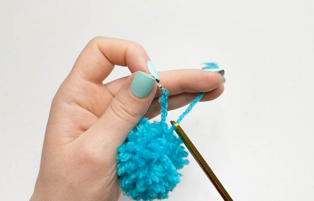Using scissors to clip off the remainder of the yarn tail from threading the pom pom onto the earring.