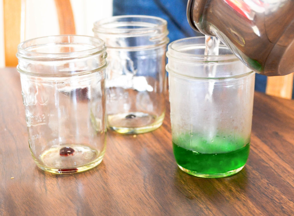 pouring the epsom salt solution into three different cups with green, blue, and red food coloring.
