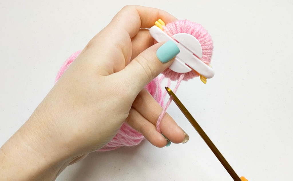 clipping the yarn between the pom pom maker and the ball of yarn.