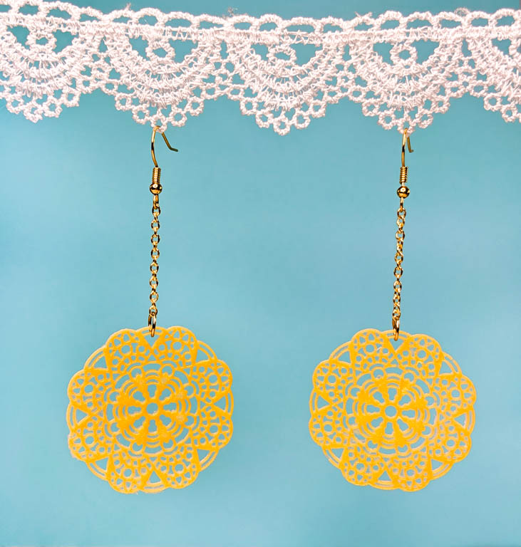 Dangle earrings displayed against a blue background hanging from white lace.