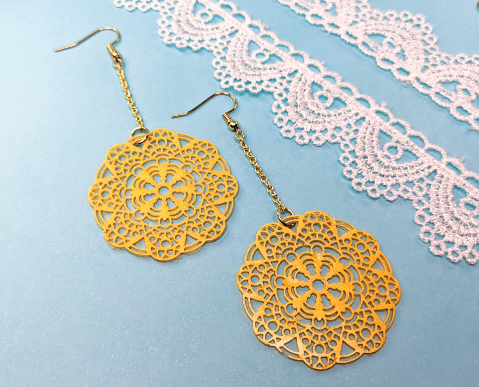 Dangle earrings displayed against a blue background next to white lace. all are displayed at a diagonal.