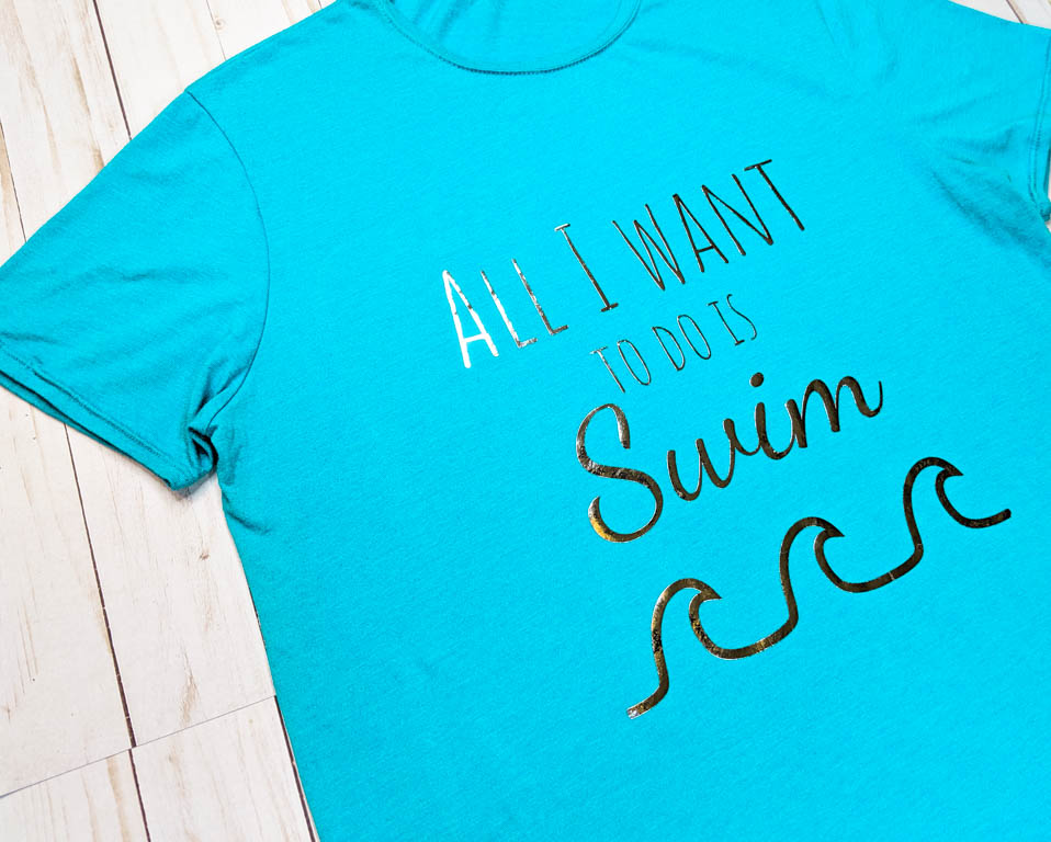 Close up shot of a blue t-shirt with the "all I want to do is swim" graphic. Features text and a graphic of a wave underneath the text.