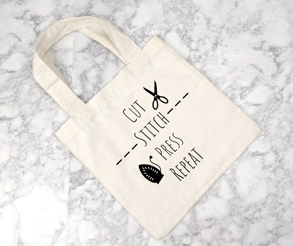 white tote bag with text "cut stitch press repeat" and images of stitching, scissors and an iron.