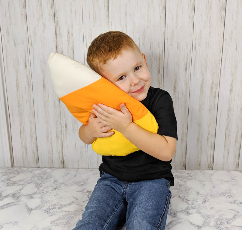 Little boy holding a candy corn pillow.