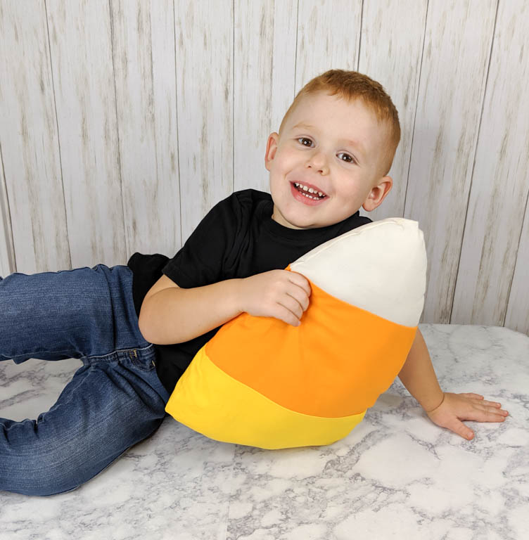 little boy holding a finished candy corn pillow.
