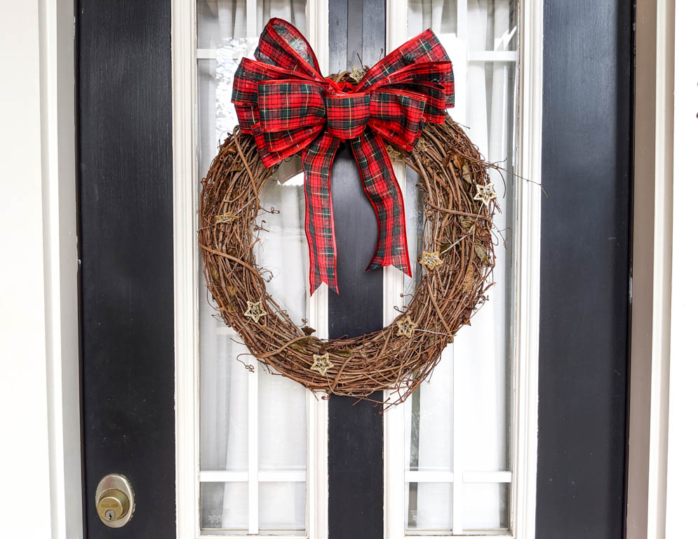 Christmas light wreath made with grapevine and with lights shaped as stars and a big plaid red bow.