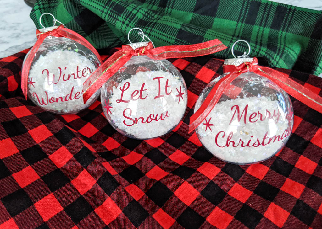 Three clear Christmas ornaments with christmas sayings on the made with vinyl. Filled with faux snow.