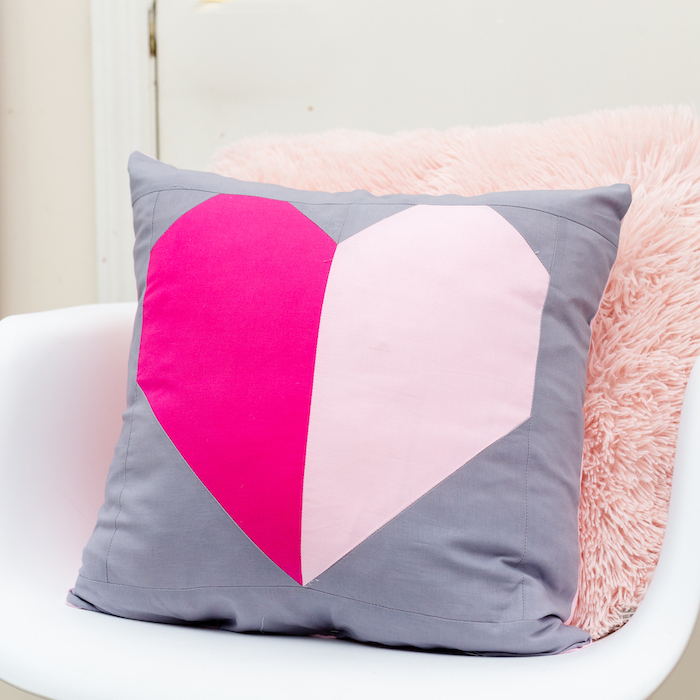 Square gray pillow with a heart blocked in its pattern.