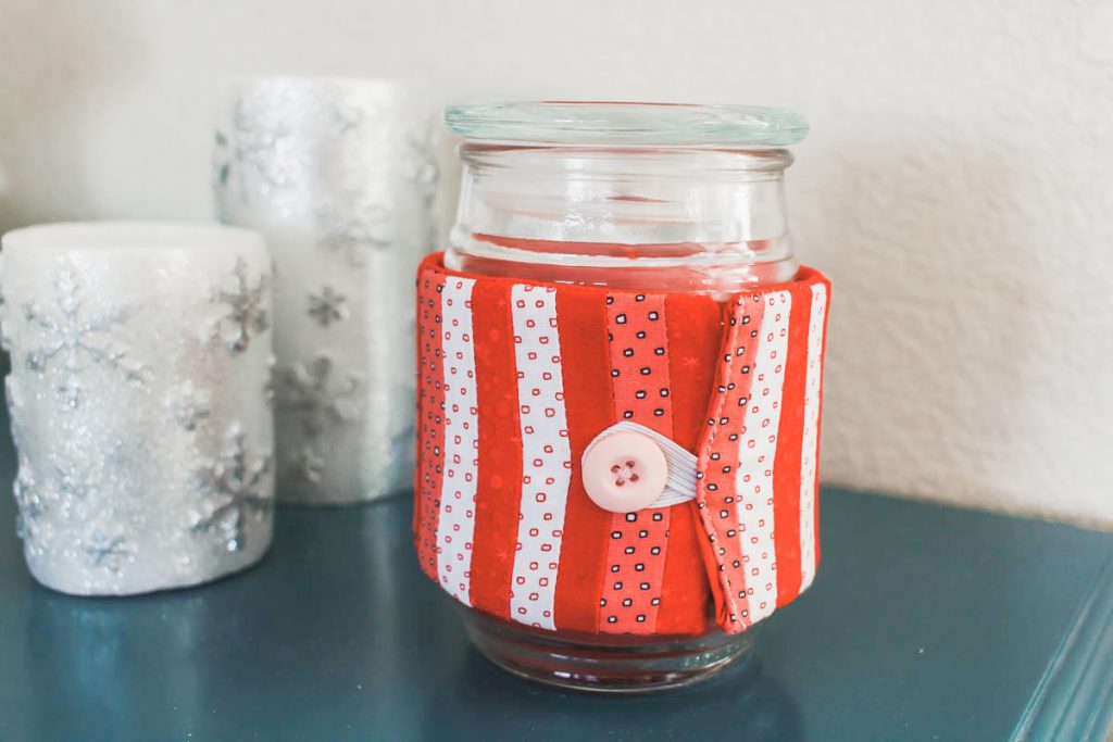 Candle wrapped in a red and white handmade cozy.