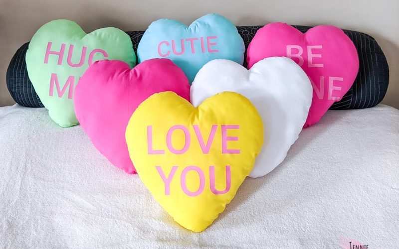 Heart pillows displayed on a bed. Some have text to look like conversation hearts.