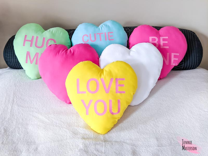 Heart pillows displayed on a bed. Some have text to look like conversation hearts.