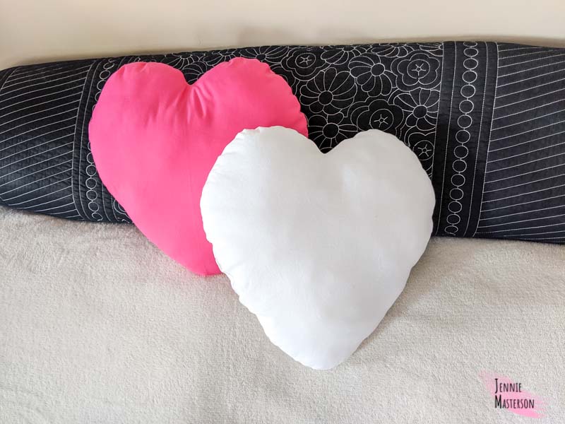 Two heart pillows on a bed, one pink, one white.