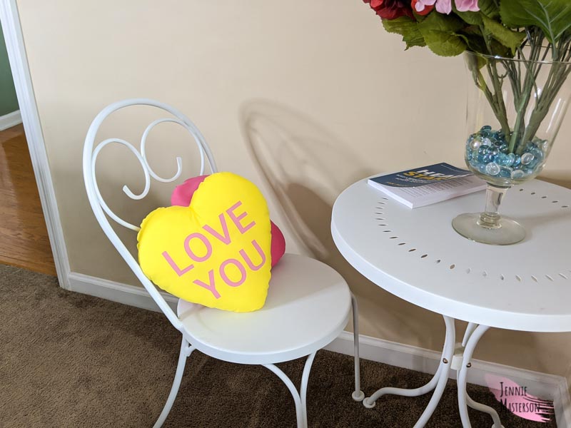 Heart pillow set on a chair of a bistro set. Heart pillow reads "Love you"