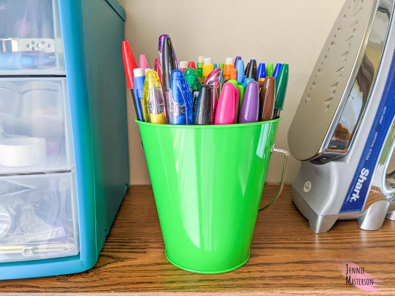 Small green bucket filled with pens.