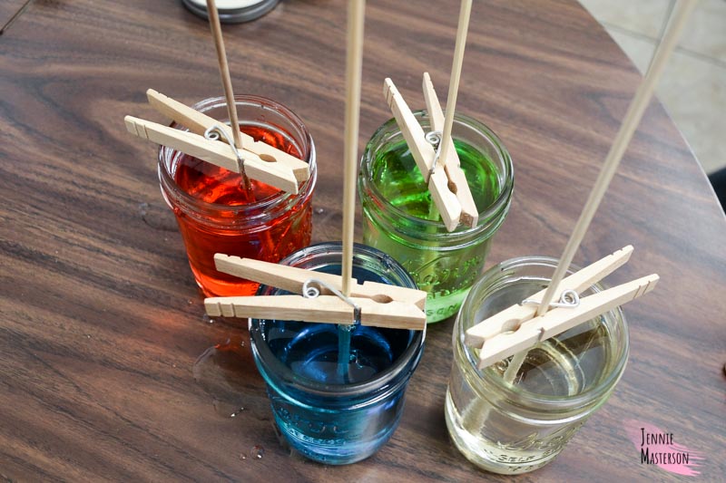 four mason jars filled with rock candy solution and have skewers placed in them.