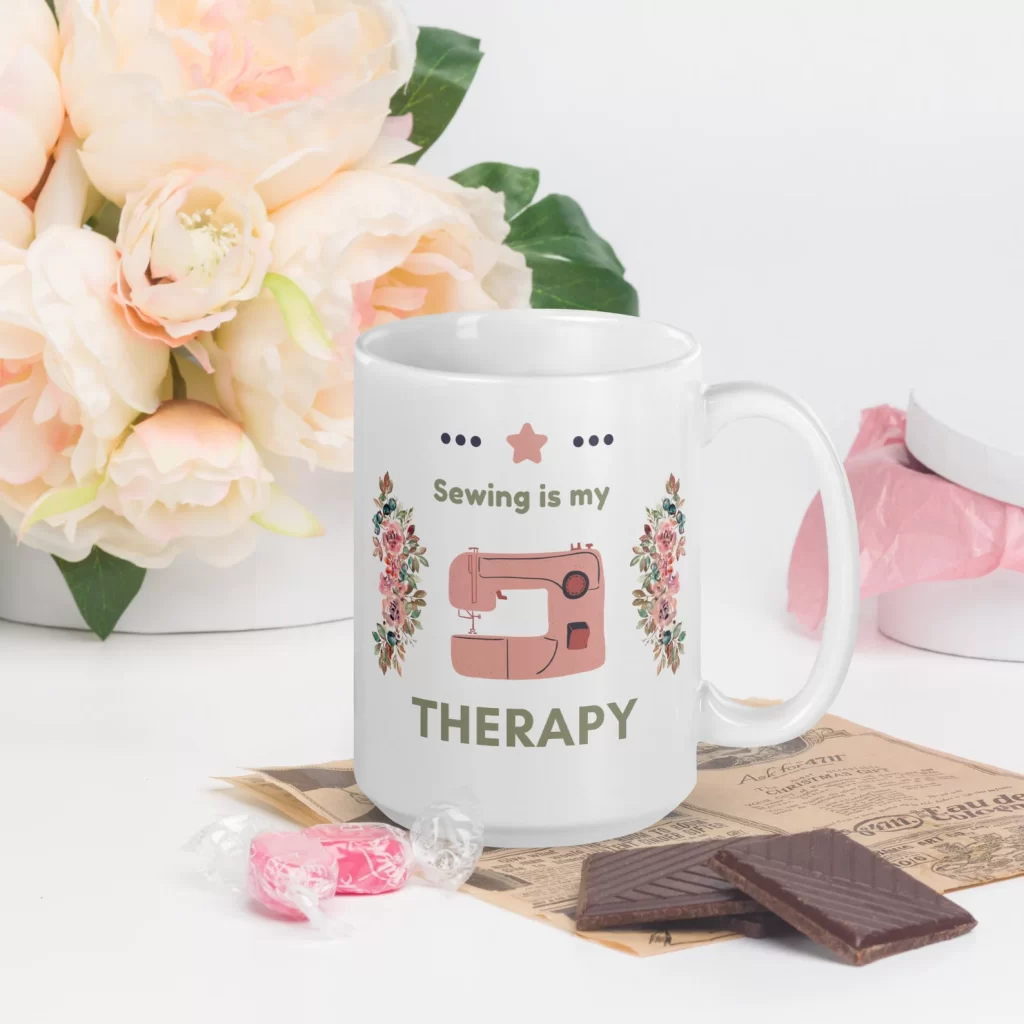White coffee mug with the words "sewing is my therapy" surrounded by flowers and a sewing machine.