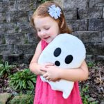 A little girl holding a white ghost plushie.