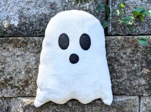 A ghost plushie against a concrete background with vines covering parts of the concrete.