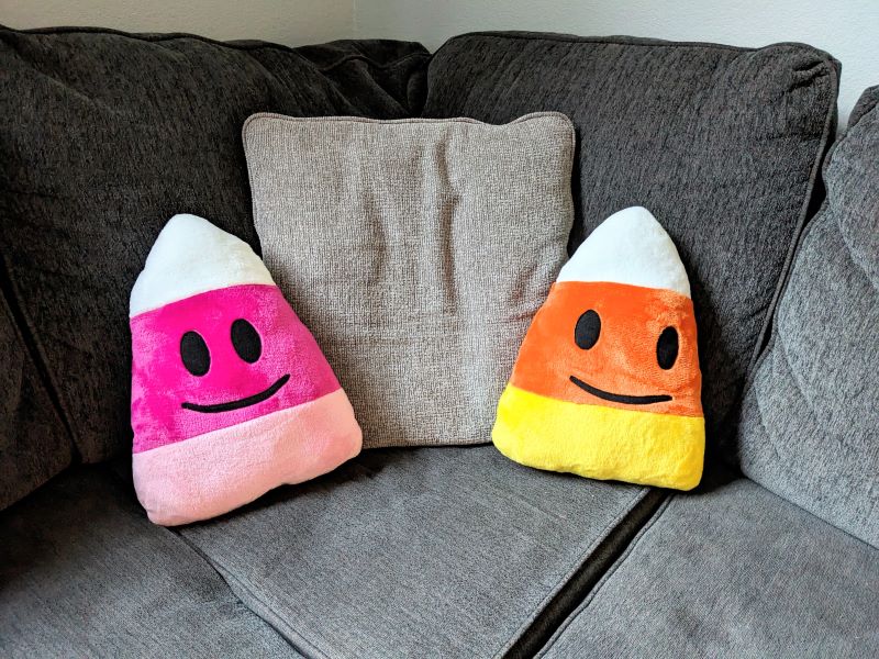 two candy corn plushies sitting on a couch.