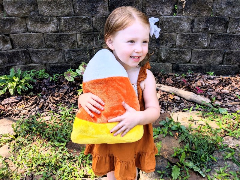 little girl holding a candy corn plushie.