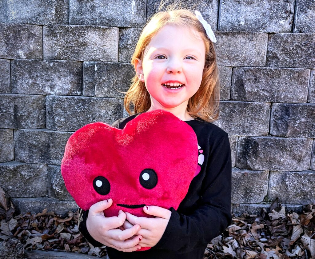 Little girl holding a red heart plushie.