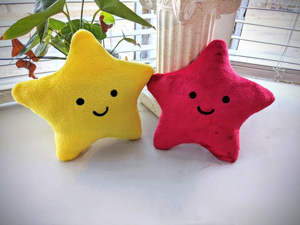 two star plushies side by side. one yellow, one red.