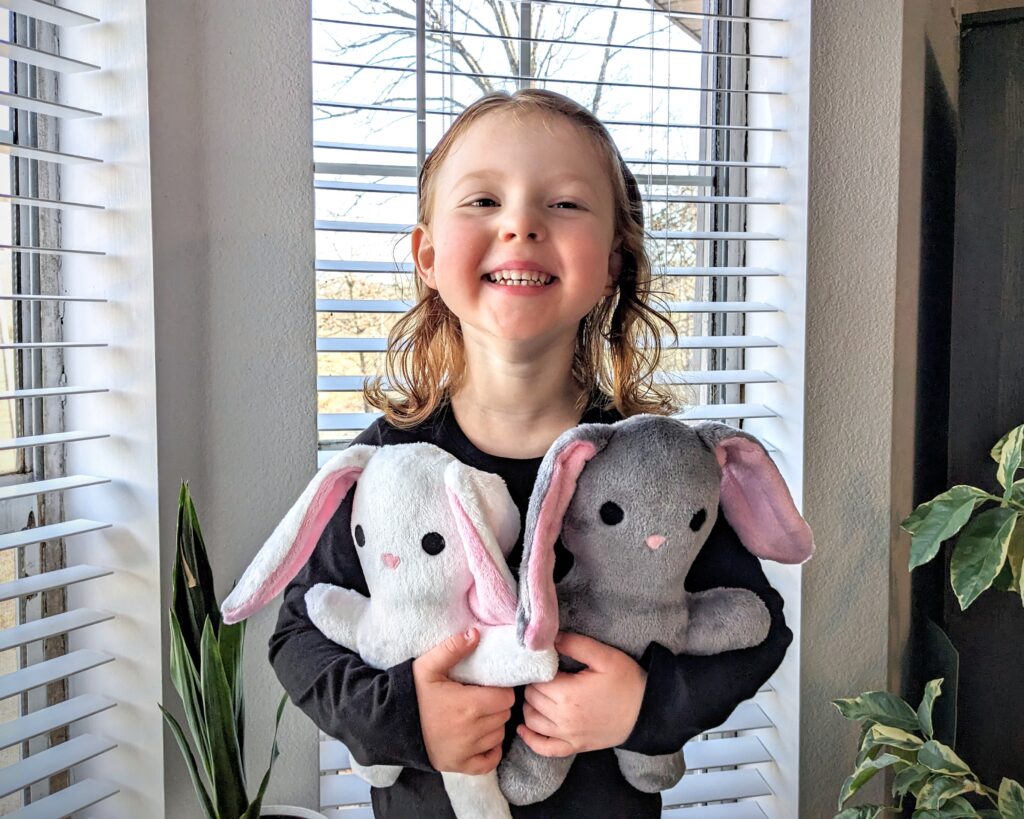 little girl holding two bunny plushies.